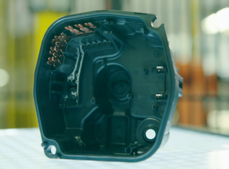 Schwarzes Kunststoffbauteil mit kupfernen Steckerverbindungen im Innern