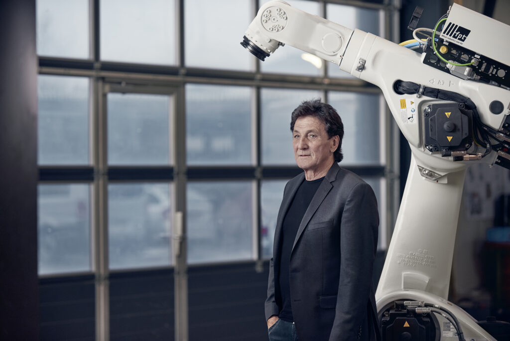 Bild Gründer und Inhaber Hermann Müller in der Produktionshalle neben einem Sechs-Achs-Roboter