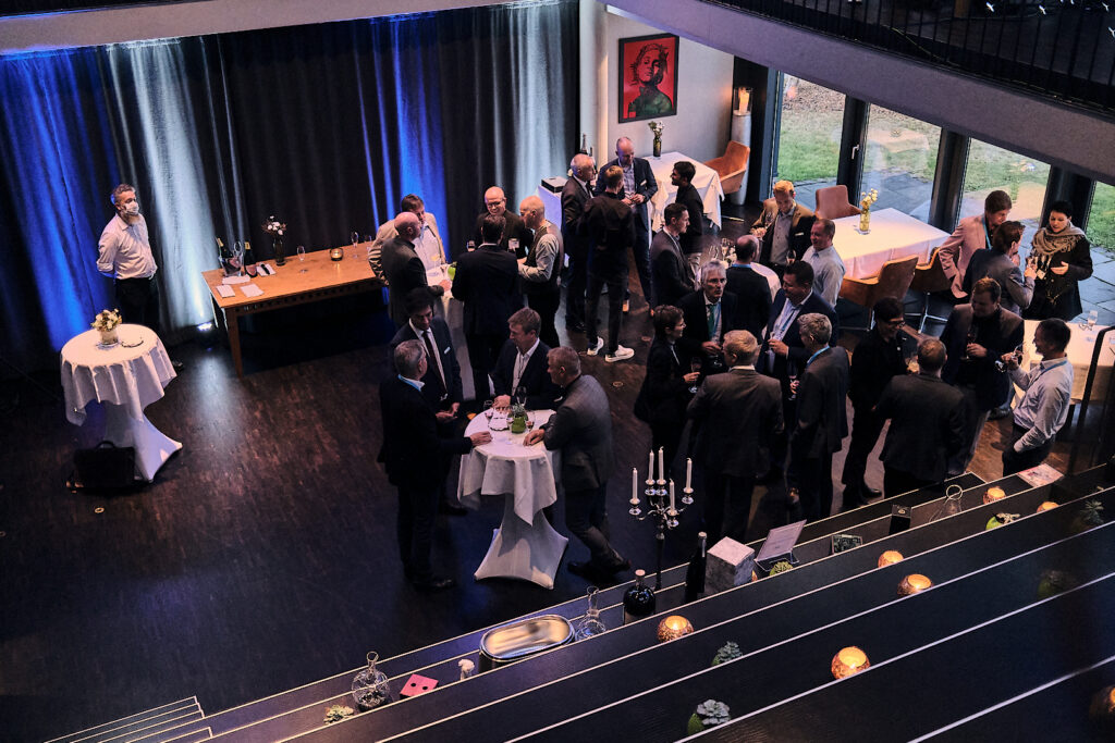 Get-together Szenerie mit Menschen im Business-Look, die sich rege unterhalten und um Stehtische versammelt sind