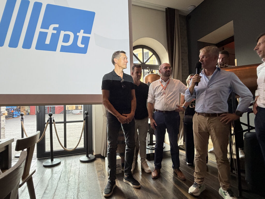 Eine hell angestrahlte Leinwand mit fpt-Logo, daneben einige Männer mit Mikro und Preis