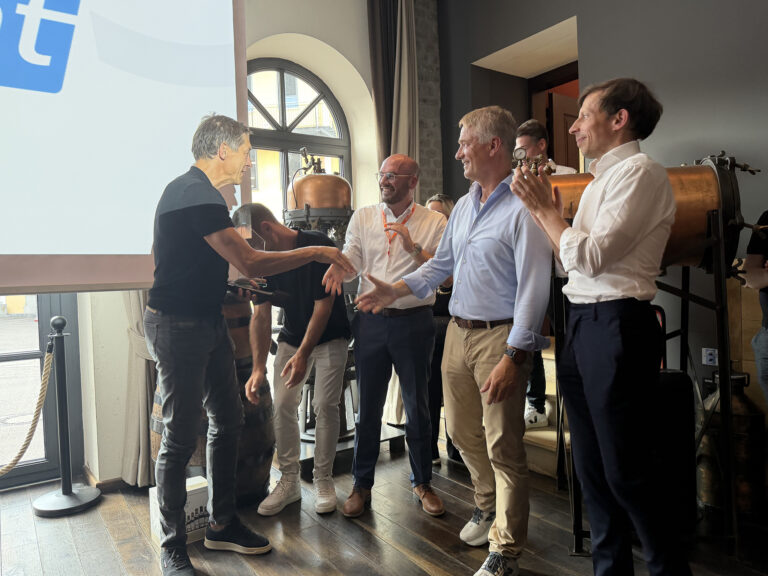 Ein Mann in schwarzem Oberteil nimmt einen gläsernen Award per Handschlag von einer Delegation Männern im Hemd entgegen