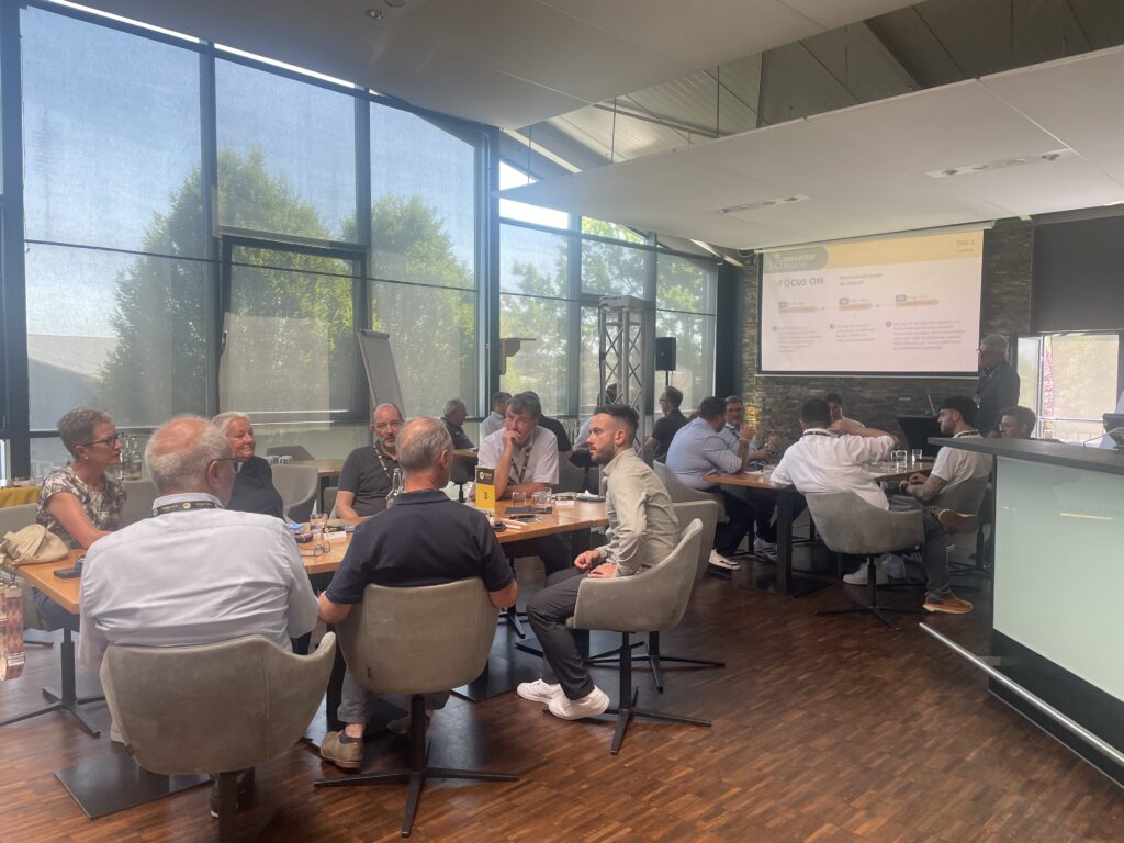 Ein Workshop mit mehreren Gruppentischen, bei dem intensiv miteinander gesprochen wird, dahinter eine helle Fensterfront