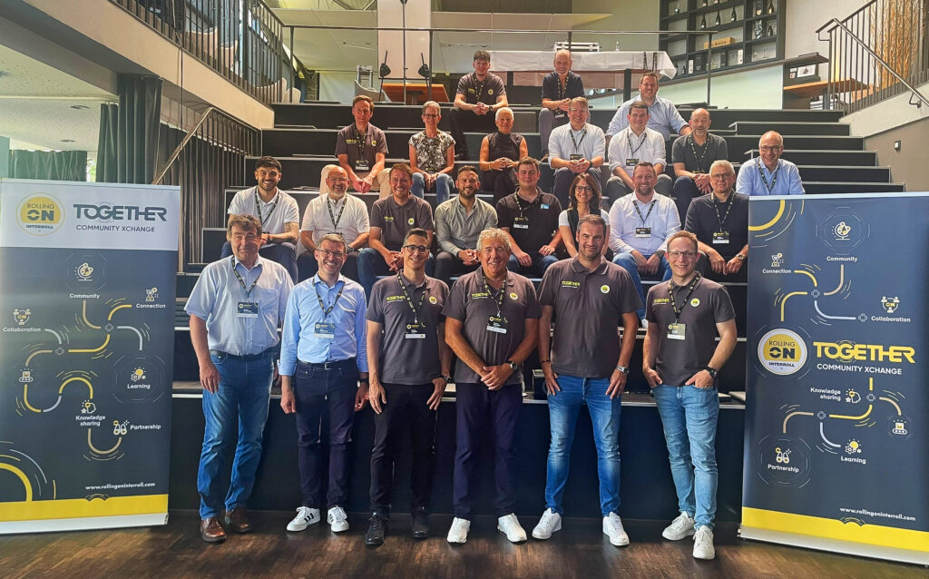 Eine Gruppe von Menschen auf einer dunklen Treppe sitzend mit Interroll-Bannern rechts und links